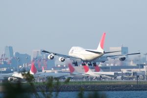 rear view of aircraft landing, with airport terminal and parked aircraft in the background.