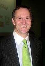 A smiling man wearing a white shirt with a green tie and black jacket