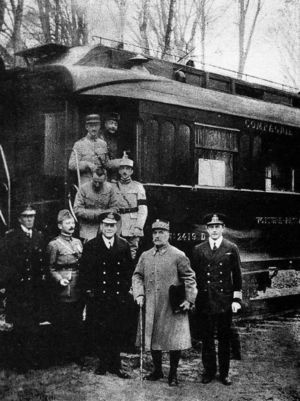 black and white photograph of five men in military uniforms standing side-to-m right, seen outside his railway carriage No. 2419 D in the Forest of Compiègne.