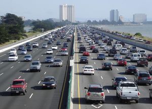 Looking down a straight busy ten-lane highway running along a coastline. In the background are a few multi-story buildings.