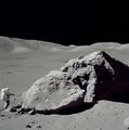 Schmitt stands next to a large boulder during EVA-3. He is looking in the direction of the LM which is visible beyond the right limb of the boulder.