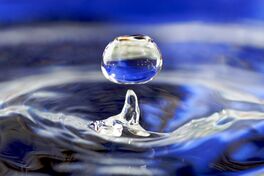 A drop of water falling towards water in a glass