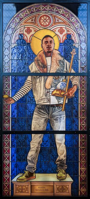 Stained glass window in a romanesque arch shape. A young black man with a golden halo, wearing modern clothes, standing on a white and gold plinth inscribed "Mark Shavers". He is holding an egg in one hand, and a book, orb and scepter in the other hand. The background is a deep blue, and the window is framed with geometric patterns