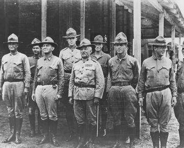 Eight people in military uniforms. They are wearing hats and are standing in formation.