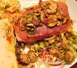 A meat and cheese sandwich with various toppings and a side dish of coleslaw