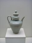 A green-tinted grey teapot with a small base and a tall body in the shape of a cone with the smallest point facing downwards. The cap covering the point that the water is poured into is a tall cylinder, and fits into a thick, wide cylindrical rim in the pot.