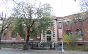 A two-story red brick building partially obscured by a tree on a cloudy day