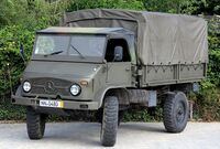 A military Unimog S 404 truck painted in camouflage in front of a forest background.