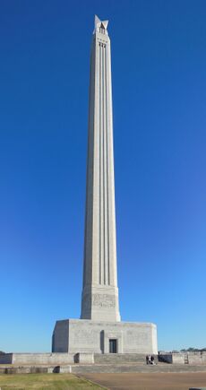 A tall stone column, which widens as it meets the base, a large rectangular building with no windows.