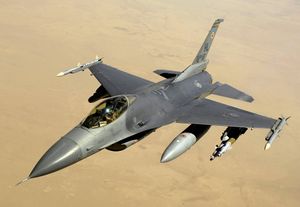 صورة جوية لطائرة نفاثة تحمل خزانات وقود اسطوانية، تحلق فوق الصحراء.