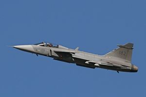 Gray jet aircraft flying right against an all-blue sky. The jet is on a shallow climbout.