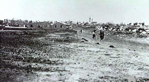 In the distance a group of people walk down a dirt road away from the village.