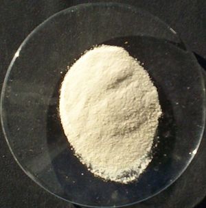 A small colorless saucer holding a pale-yellow powder