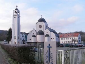 Modern monastery building with white walls and bell tower surrounded by trees