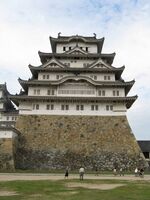 A large castle tower with white walls and dark roofs on a platform of unhewn stones.