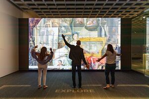 Three museum visitors strike different poses as they interact with a digital ARTLENS display.