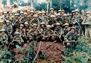Men in military camouflage, wearing helmets, carrying long guns, and shouting