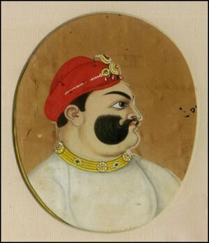 A color portrait of a mustached man, from the chest up, wearing a crown